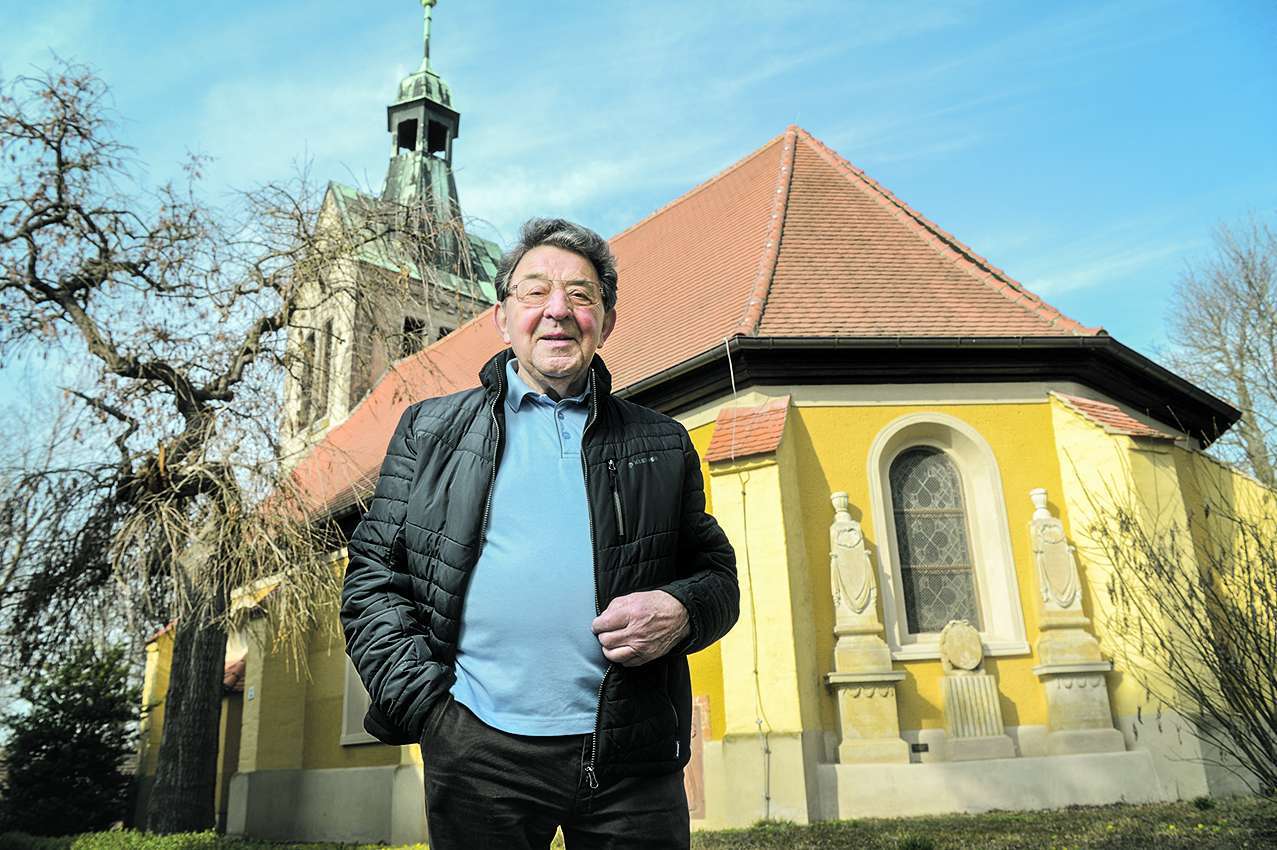 Stütze der Gemeinde: Willy Schröter vor der Kirche in Schortewitz. Auch für die Restaurierung der beiden Stelen, die im Hintergrund zu sehen sind, hat er sich eingesetzt.