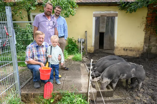 Karl und Gerhard Weinländer mit Enkel Noah und Pfarrer Christian Dellert (v.l.n.r.) am Gehege der Duroc-Schweine Lina, Frederick und Tinkia. | Foto: epd-bild/Timm Schamberger