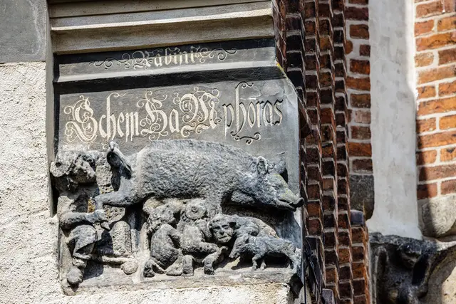 Mittelalterlichen Schmähplastik  an der Stadtkirche Wittenberg. Das Spottbild auf die jüdische Religion befindet sich seit etwa 1290 an der Südostecke der Stadtkirche St. Marien. 

Eine 1988 vor der Kirche eingelassene Bodenplatte und eine Stele mit Erläuterungen stellen die Plastik in einen distanzierenden Kontext.  | Foto: epd-bild /Jens Schlueter