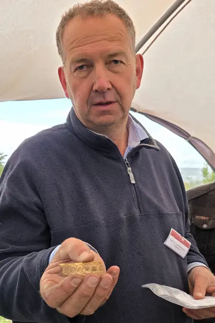 Ausgräber Felix Biermann mit einem kunstvoll verzierten Plättchen (wohl Geweih oder Knochen), das wohl einstmals ein Reliquien- oder Schatzkästchen zierte.