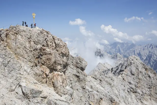 Garmisch-Partenkirchen (epd). Der höchste Berg Deutschlands bekommt ein zweites Gipfelkreuz. Damit wolle man gefährliche Situationen rund um das Original auf 2.962 Meter entschärfen, sagte die Pressesprecherin der Bayerischen Zugspitzbahn, Laura Schaper.
«Wir haben jährlich rund 600.000 Gäste aus aller Welt am Gipfel, aber das Gelände rund ums Kreuz ist sehr beengt und abschüssig», sagte Schaper. Das zweite, originalgetreue Kreuz werde am 3. Juli neben der historischen Ausstellung «90 Jahre Zahnradbahn» in der Gipfelstation vor einer Wand mit Bergpanorama aufgestellt. Dort könnten Gäste dann in Ruhe und ohne Absturzgefahr ihr «Gipfelfoto» machen.
Trotz des Andrangs am Originalkreuz käme es insgesamt zu wenig Unfällen, sagte die Pressesprecherin. Dennoch beobachte man die Situation mit Sorge. Immer wieder müsse die Bergwacht Menschen helfen, die - zum Teil nur mit Turnschuhen und Flipflops ausgestattet
- in dem steilen, felsigen Gelände nicht mehr weiterkämen. Zudem werde es immer beliebter, sich am Gipfelkreuz mit Stickern zu verewigen. «Weil aber im unteren Bereich kaum noch Platz ist, versuchen viele, möglichst hochzukommen» - ein weiterer Gefahrenpunkt, sagte Schaper.
Auch wenn das «Zweit-Kreuz», das der ortsansässige Künstler Bernhard Rieger gestaltet hat, in den Räumen der Gipfelstation steht, sei das perfekte Selfie dank Fotowand möglich - künftig sogar, wenn der Zugspitzgipfel in Wolken steckt. Daneben sollen die Gäste etwas über die Geschichte des Kreuzes erfahren, das 1851 auf Initiative des Hohenpeißenberger Pfarrers Christoph Ott und mit Unterstützung der Königin Marie von Bayern (1825-1889) aufgestellt wurde.
 | Foto: epd-bild/mck